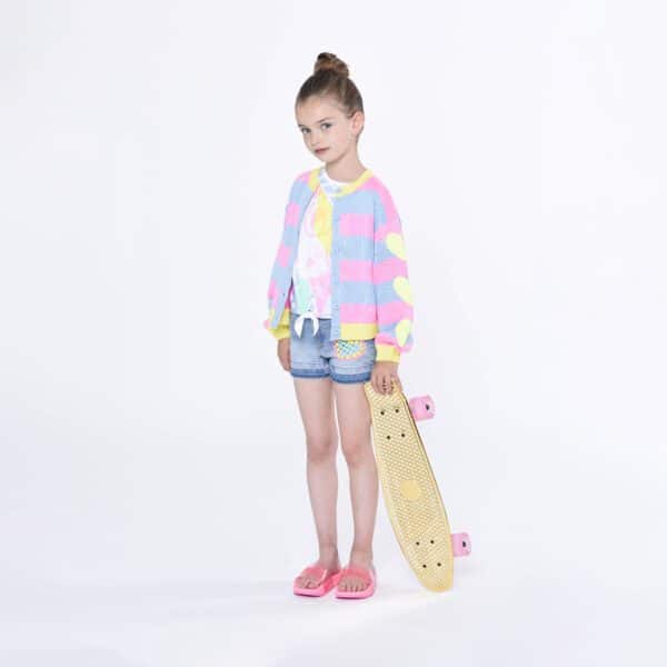 Billieblush model in multi coloured cardigan with skateboard