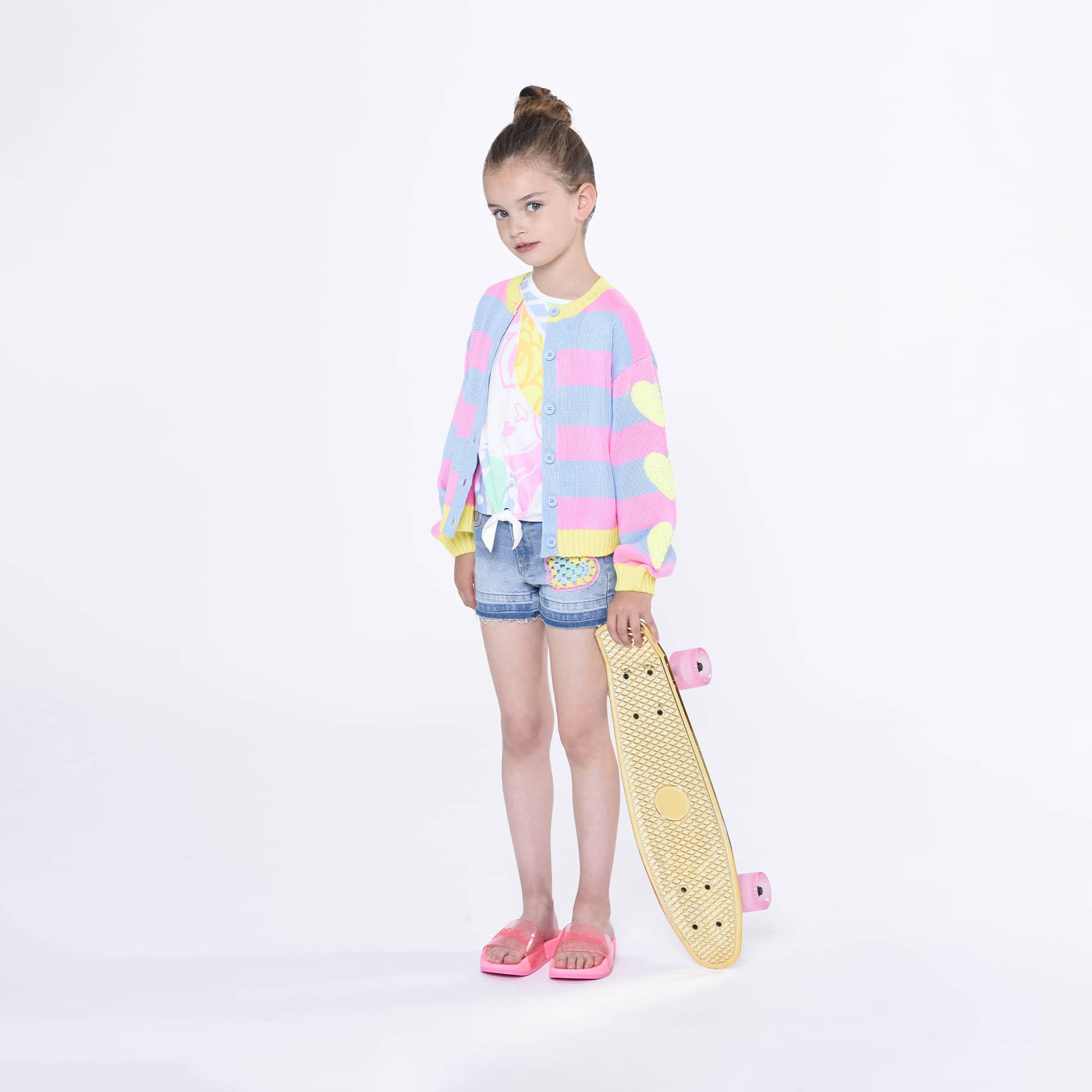 Billieblush model in multi coloured cardigan with skateboard